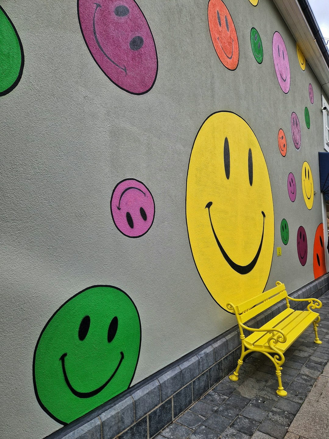 Wall with colourful smiley faces and a yellow bench, symbolising positivity and success habits.
